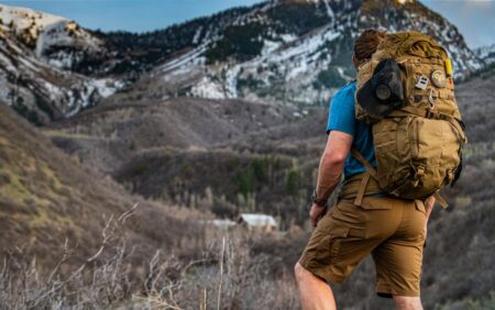 Hiker with large tactical backpack overlooking snowy mountain valley landscape