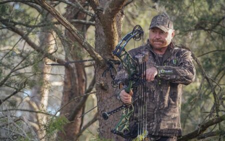 Hunter in camouflage holding compound bow in wooded forest setting outdoors.