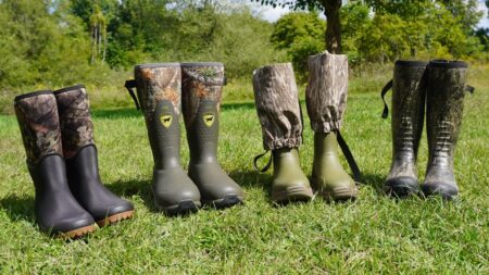Four pairs of hunting rubber boots in camouflage patterns displayed on green grass outdoors.