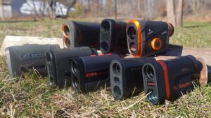 Six laser rangefinders from Vortex, Ravin, and Maven brands displayed outdoors on wood