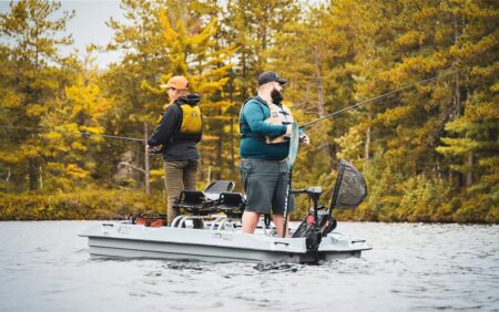 Two anglers standing on a small fishing boat casting rods on a lake.