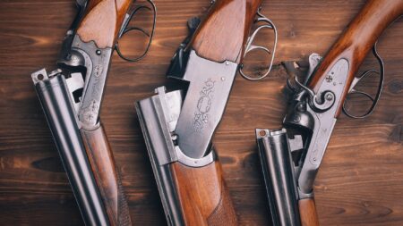 12 Gauge vs 20 Gauge for Hunting Just About Anything Three vintage double-barrel shotguns with engraved receivers and wooden stocks on wooden surface.