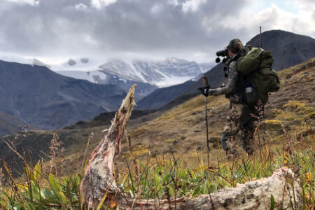 An Executive Order from President Trump Could Strip Protections from Millions of Acres of Prized Hunting and Fishing Grounds in Alaska Hunter with binoculars scouts alpine mountain terrain near animal bones in wilderness