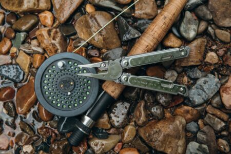 Leatherman multi-tool and fly fishing reel with rod on wet river rocks