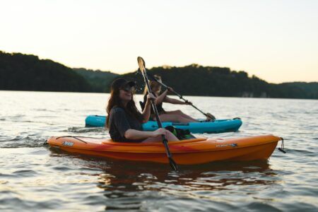 Two women kayaking on a calm lake at sunset in colorful kayaks.