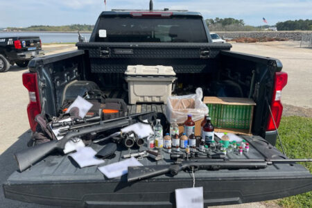 Truck bed displaying seized firearms, chemicals, and various bottles during law enforcement operation.