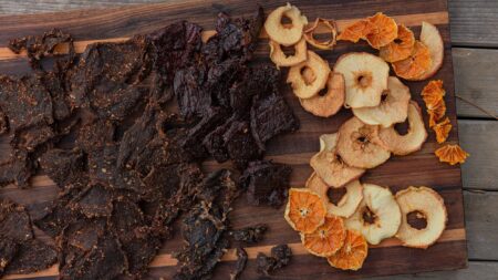 Dehydrating Food: Why to Do it, How to Start Beef jerky and dehydrated apple and orange slices arranged on wooden cutting board