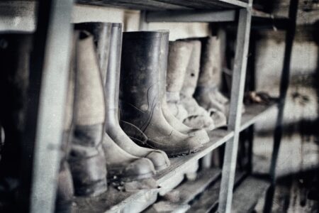 Worn rubber work boots lined up on metal storage shelves in workshop