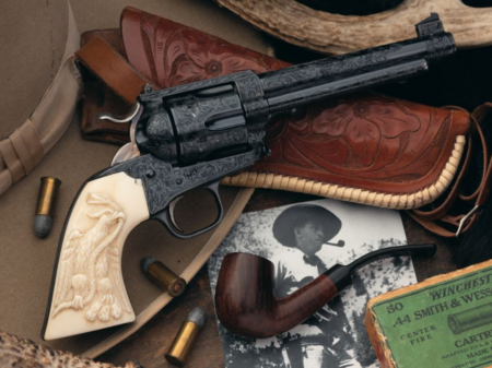 Engraved Colt Single Action Army revolver with ivory grips beside Winchester 44 ammo box