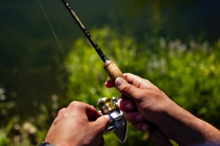 The 6 Best Ultralight Spinning Reels Hands holding a spinning fishing rod and reel near a green riverbank