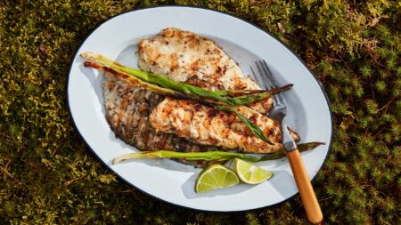 The Secret Ingredient for Perfectly Cooked Fish Grilled fish fillets with charred scallions and lime wedges on white plate outdoors