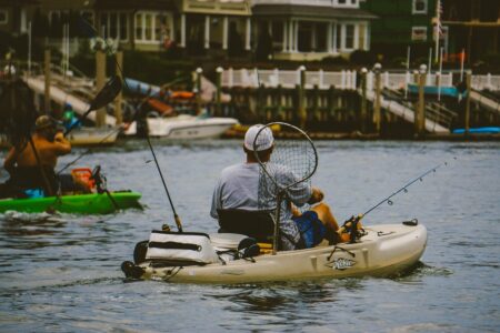 Man fishing from Hobie kayak with net and rods in marina waterway.