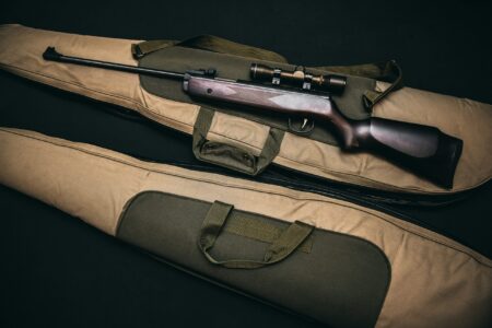 Scoped rifle with wooden stock resting on two tan and olive gun cases