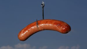 Cooked bratwurst sausage hanging on a fishing hook against blue sky