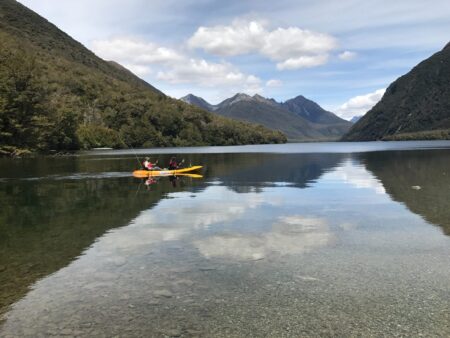 The Best Kayak Paddles for Fishing (2024 Guide) Two people kayaking on a calm mountain lake with stunning reflections in New Zealand.