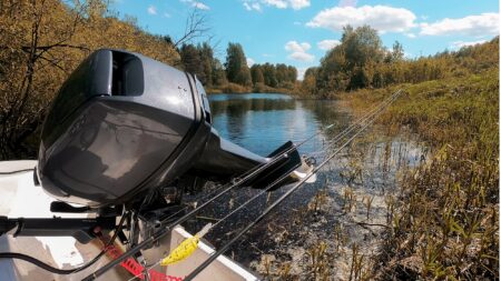 Outboard motor on small boat in calm river surrounded by autumn trees