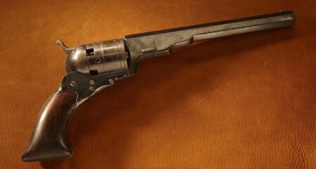 Antique Colt revolver with wooden grip displayed on brown leather surface