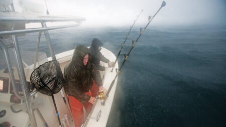 Two fishermen in rain gear fishing from a boat in rough foggy seas.
