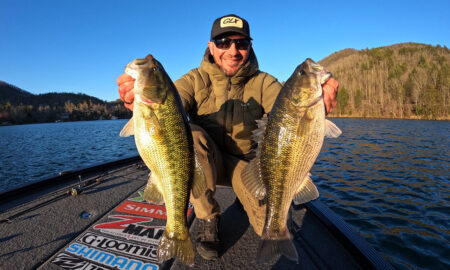 The 8 Best Winter Bass Lakes, According to The Pros Angler holding two large bass fish on a boat at a mountain lake.