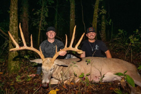 Bowhunter Tags Giant Missouri Whitetail with 29-Inch Main Beams and 25-Inch Spread Two hunters posing with a large trophy whitetail buck in the woods at night.