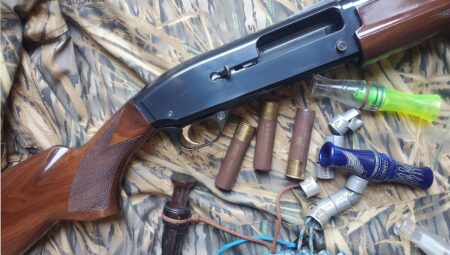 Pump-action shotgun with various shotgun shells and duck calls on camouflage fabric