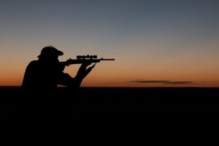 Silhouette of hunter aiming rifle against vibrant orange and blue sunset sky