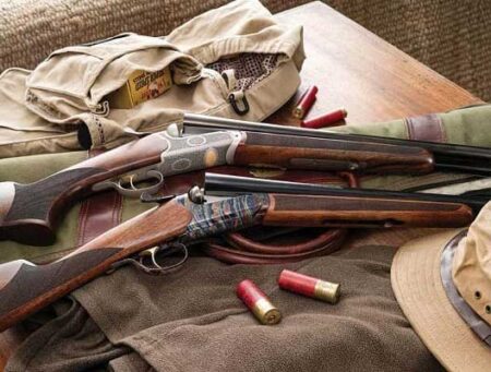 The 10 Best Shotguns for Hunting Rabbits Two over-under shotguns with spent shells and hunting gear on wooden table.