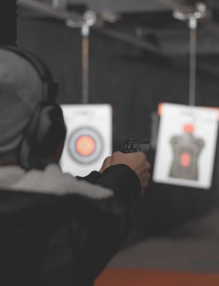 Person wearing ear protection aiming handgun at targets in indoor shooting range