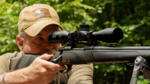Man aiming bolt-action rifle with GPO scope outdoors wearing Mars Hill cap