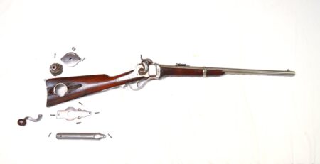 Antique rifle partially disassembled with components laid out on white background