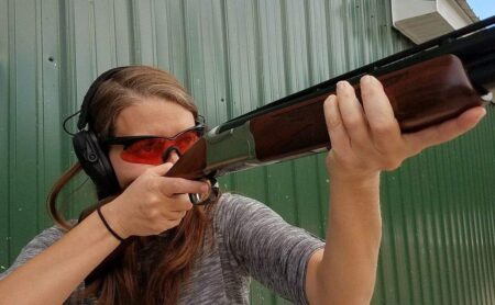 Young woman aiming shotgun at shooting range wearing ear protection and safety glasses