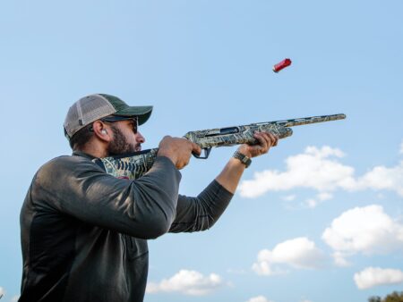 Customize Your Shotgun’s Fit for Mere Pennies Man firing camouflage shotgun outdoors with ejected shell casing visible in air