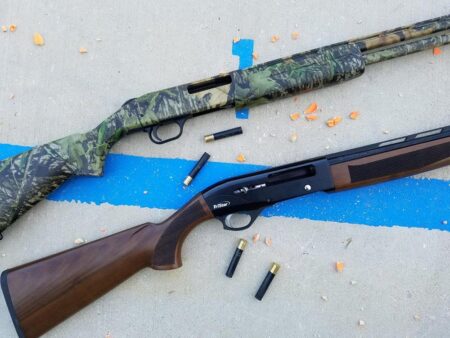 Two shotguns with spent shells on concrete, one camouflage and one TriStar wood stock.