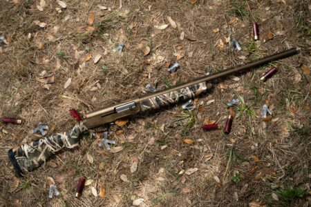Shotgun Review: The Browning A5 Wicked Wing Camouflage shotgun lying on ground surrounded by spent red shotgun shells outdoors.