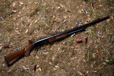 Pump-action shotgun with spent shell casings on autumn ground outdoors