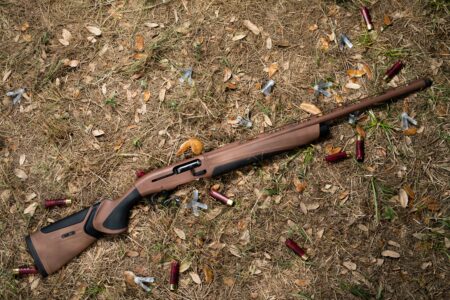 Brown semi-automatic shotgun lying on ground surrounded by spent shotgun shells