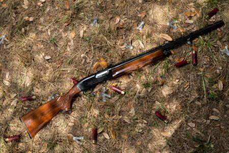 Vintage pump-action shotgun with wooden stock lying on ground surrounded by spent shells.