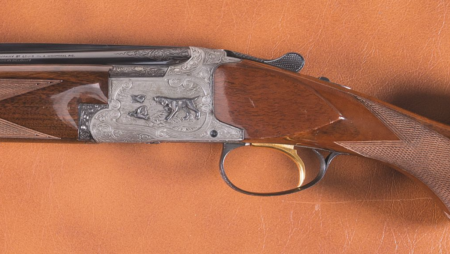 The 5 Worst Shotguns Ever Made Engraved over-under shotgun with walnut stock and gold trigger on leather surface