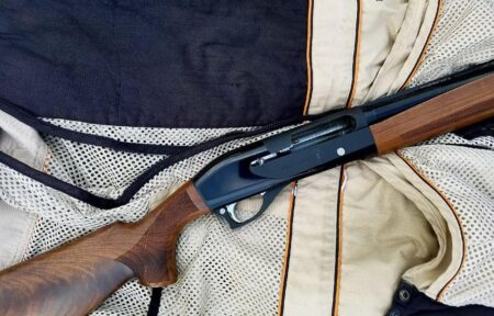 Semi-automatic shotgun with wooden stock resting on a hunting jacket