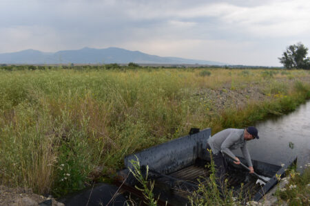 Man operating irrigation gate on rural canal with mountain backdrop
