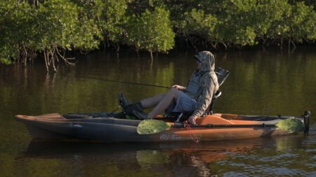 First Look: The New Old Town Electric Pedal Assist Kayak Will be a Game Changer for Anglers Person fishing from an Old Town kayak on calm water near mangroves.