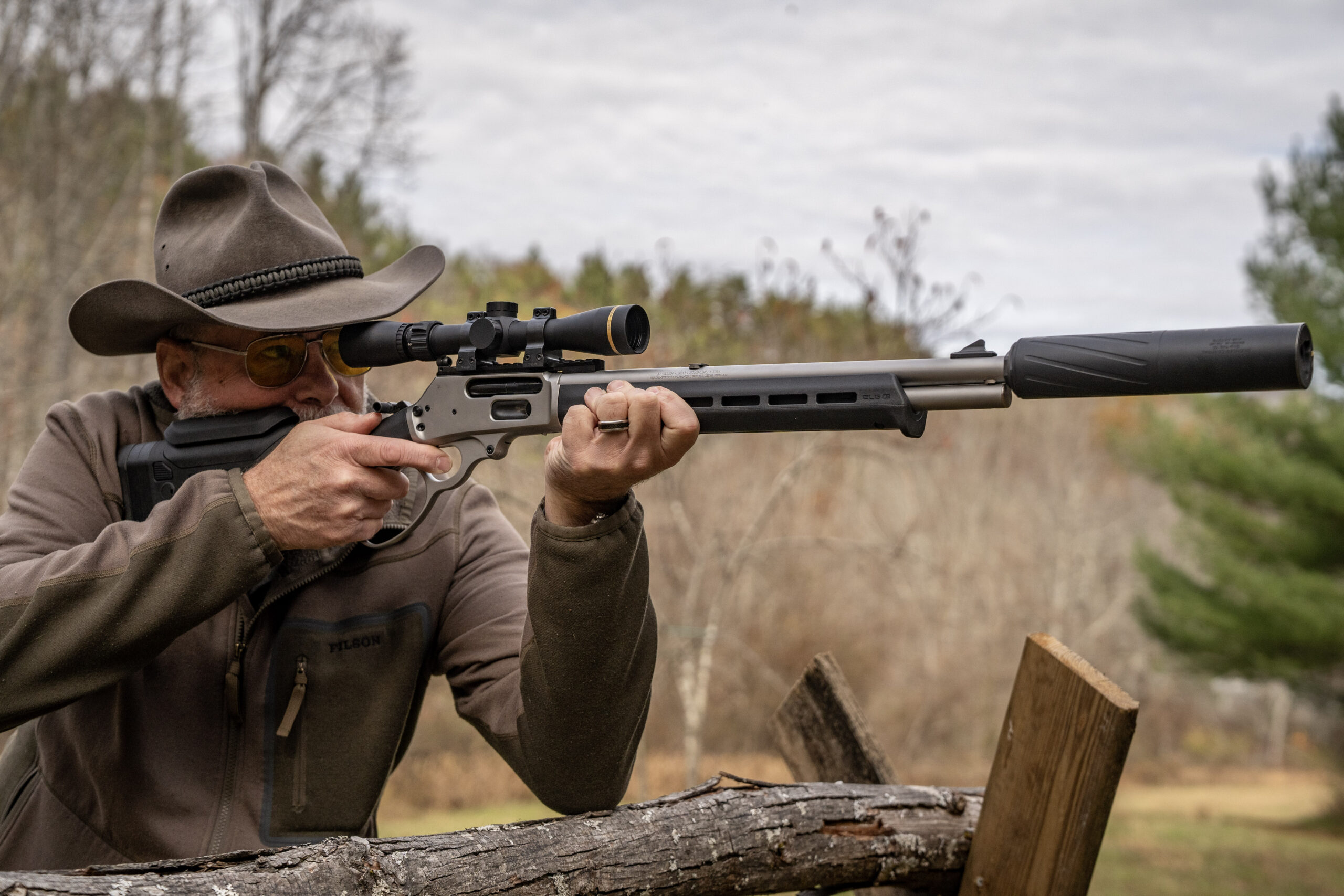 A shooter fires a scoped lever action rifle with a suppressor.