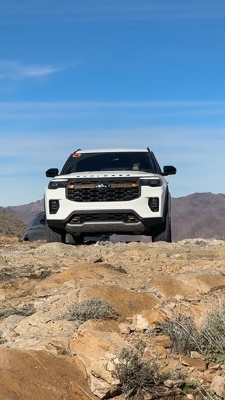A white SUV peaks over a desert hillside