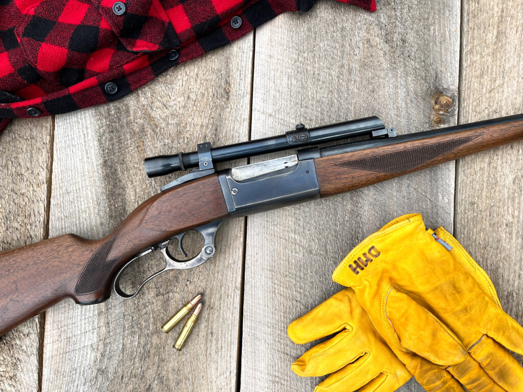 A Savage 99 rife laying on boards with ammo, glove, and shirt. 