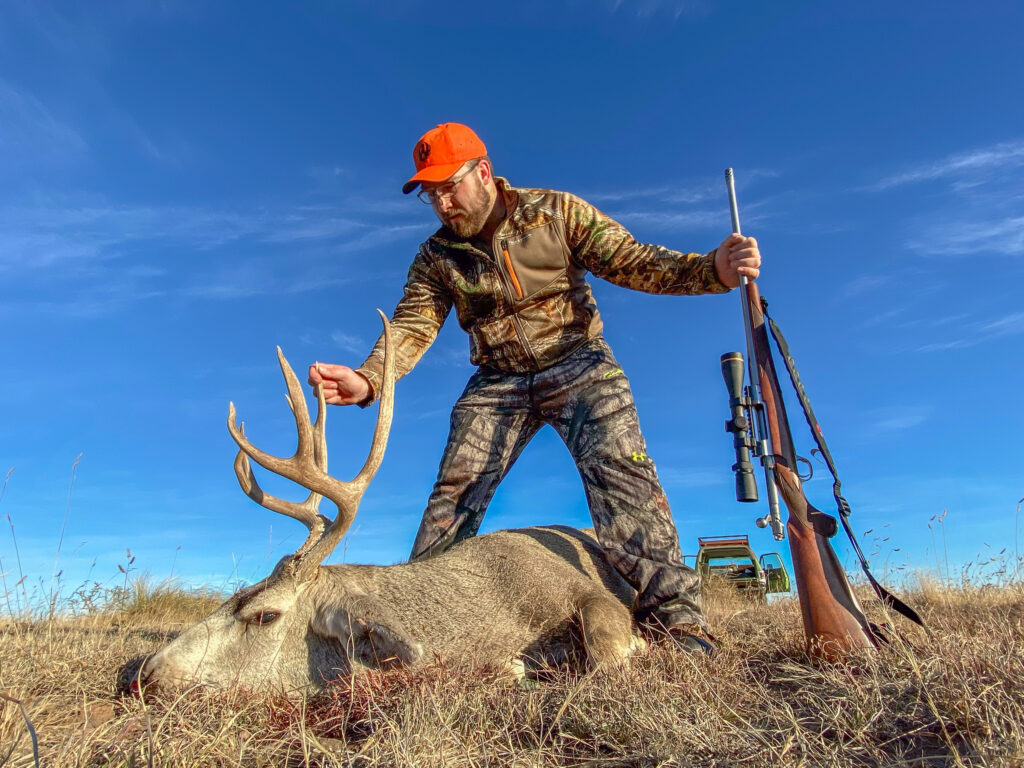 A hunter admires a mule deer he shot with a rifle.