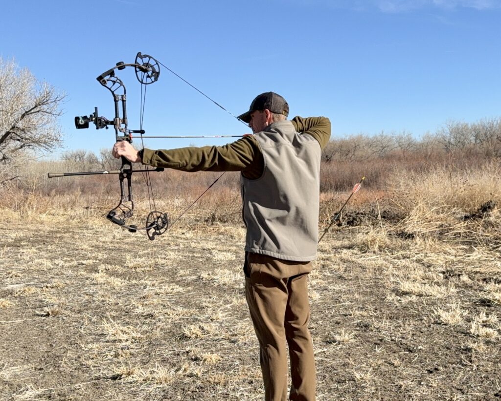 An archer draws back the new Prime Divide compound bow in a field. 