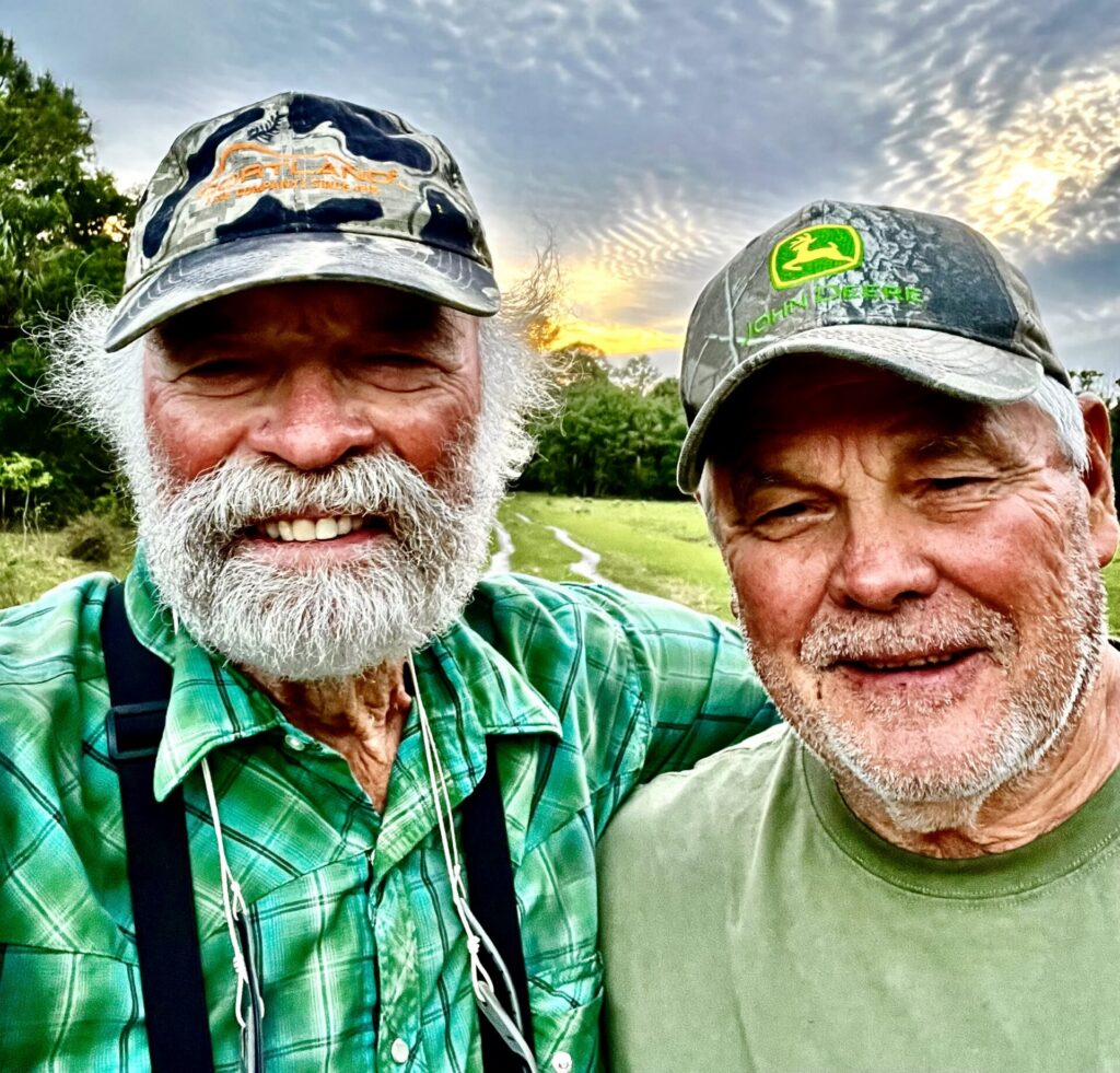 Flip Pallot stands next to a man in a hat and green shirt beneath a blue sky.