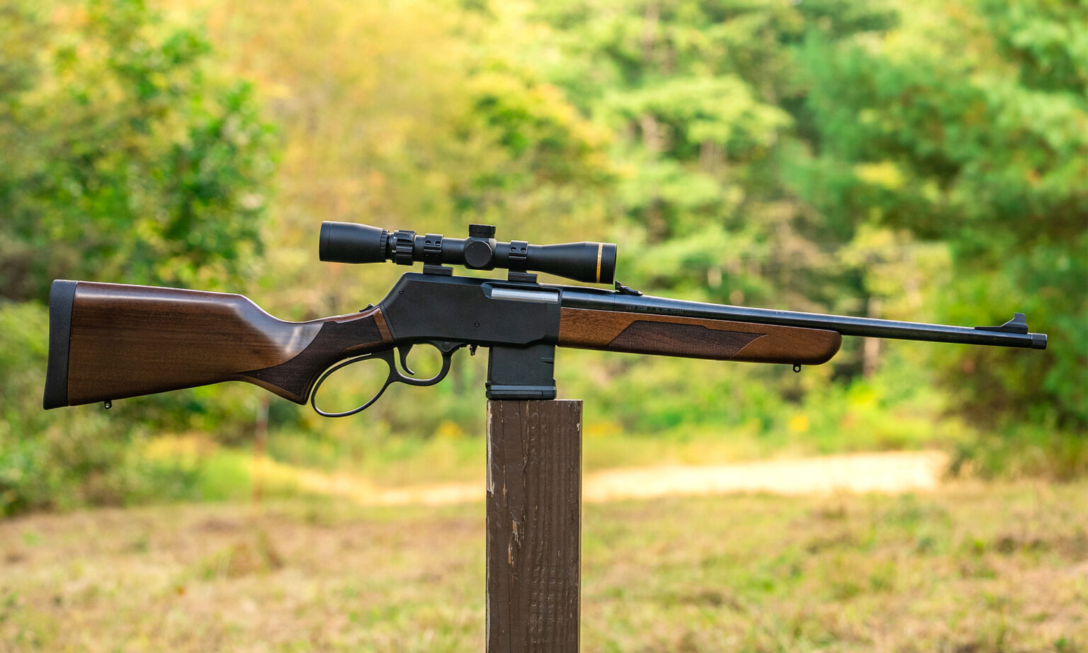 Henry Lever Action Supreme rifle balanced on a post in a field.
