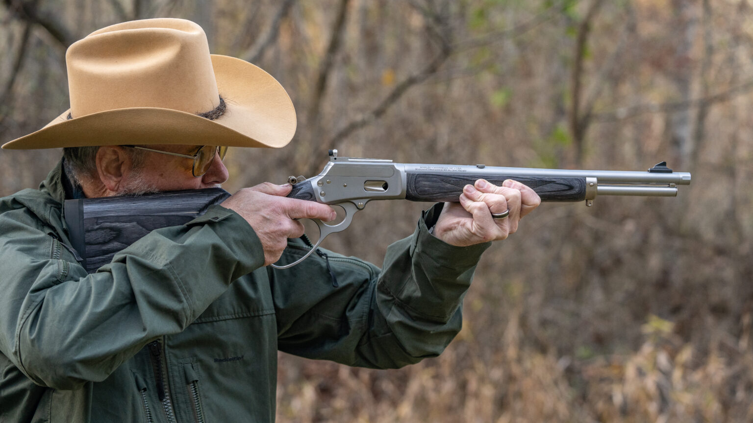 A man in a cowboy hat shoots a lever-action rifle