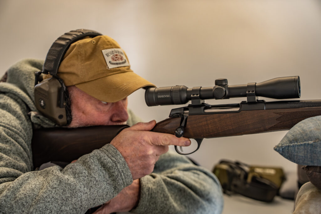 A shooter fires a rifle from a bench rest.